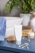 White cream tube near personal care products on blue bath countertop close up, cosmetic mockup