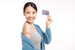 young asian women smiling after getting a vaccine, and show credit card holding down her shirt sleeve and showing her arm with bandage after receiving vaccination on white background,
