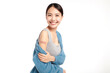young asian women smiling after getting a vaccine, holding down her shirt sleeve and showing her arm with bandage after receiving vaccination on white background,