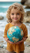 Young child holding a globe at the beach, symbolizing hope and environmental education. World Ocean Day.