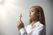 Young Asian Christian woman hand holding wooden holy cross and praying with strong faith in Christianity