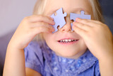 Fototapeta Na ścianę - happy cool trendy funky girl looks cheerfully into camera, happy child 4 years old creates glasses from puzzle pieces, concept of vision examination, emotional development of children
