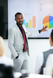 © peopleimages.com - Black man, coach and chart with screen for presentation, meeting or corporate statistics at seminar. Businessman, manager or speaker talking to group of employees on company revenue, growth or profit