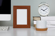 Empty picture frame on table in workspace with computer, coffee cup and desk clock