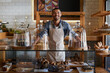 © peopleimages.com - Coffee shop, portrait and happy man waiter in bakery for store welcome, help and friendly hospitality service. Retail, startup and cafe or restaurant server with cake, cookies or counter assistance