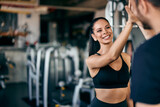 Fototapeta Pomosty - Focus on the smiling girl, giving a high five to her male partner, finishing a workout together, at the gym.