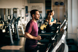 Fototapeta Pomosty - Focus on the tired male runner, running on a treadmill, at the gym.