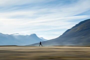 Canvas Print - Individual briskly walks through an expansive field, with towering mountains as backdrop, A figure moving swiftly across a vast landscape