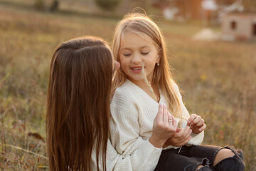 Wall Mural - Family day, mother's day. Happy smiling young mom and adorable child daughter soft hugging, kissing and spending time together at autumn on sunset. Idyllic family having fun outdoors on fall holiday.