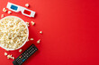 Indoor movie fest with delectable snacks. Top view vertical image showcasing popcorn, 3D glasses, remote. Vibrant red background, ideal for text or promotional content