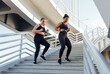 Two female friends with different body types wearing black sportswear and running down the staircase. Young women exercising together on a staircase.