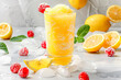Lemon slushie in glass with fruit and crushed ice around it on white marble