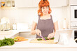 © VICTOR - A woman is cutting vegetables on a cutting board in a kitchen. She is wearing an apron and has a tablet in front of her