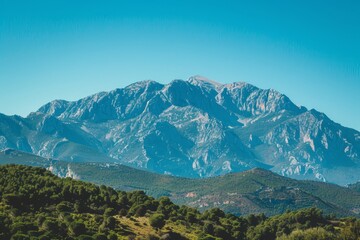 Sticker - A breathtaking view of a majestic mountain range with lush trees in the foreground, set against a clear blue sky, A majestic mountain range under a clear blue sky