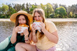 Two girls by the water, in nature, happy, eating hamburgers on a dock