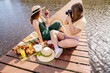 Two women enjoying a picnic by the lake, one capturing the moment with a photo