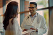 © Ikhou - Prompt: A male doctor talks to a patient, wearing a white coat and glasses, holding medical records, standing at a hospital window with an indoor light and warm colors, smiling