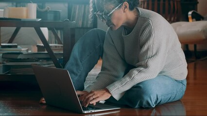 Wall Mural - An attractive woman sitting on the floor at home smiles, looks at her laptop screen and works. Relaxed female in her living room reading emails. Technology concept. Browsing the web on computer