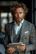 A trendy and glamorous businessman with a tablet exudes confidence in a modern corporate setting.
