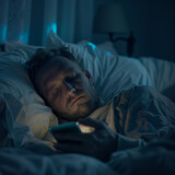 Fototapeta  - Hombre acostado en la cama sin poder dormir en medio de la noche mirando su teléfono con todas las luces apagadas