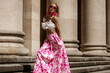 Elegant, stylish woman in pink floral dress and sexy high heels is sensually walking in the city on a sunny summer day. Outdoor shoot.