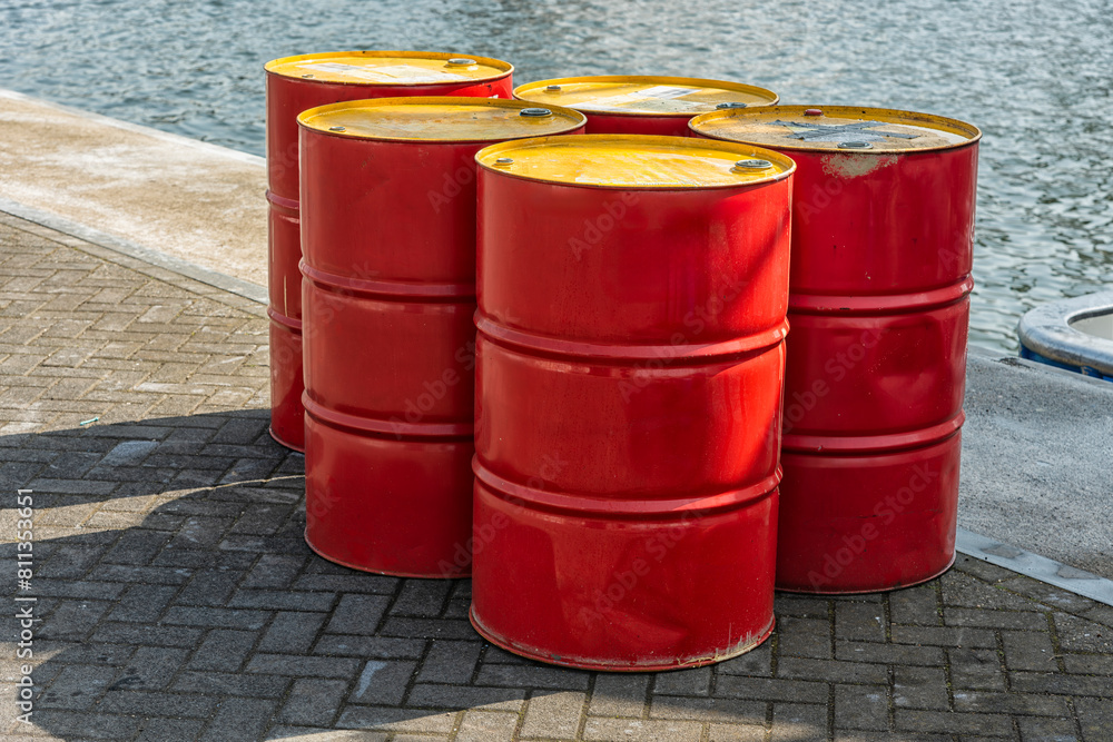 five red oil barrels with yellow steel lids stand outside on the harbor quay