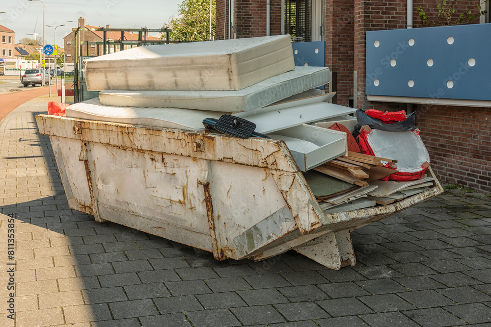 open steel industrial waste container filled with household waste and mattresses