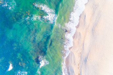 foam from waves on the shore of a beach without people, overhead view with drone