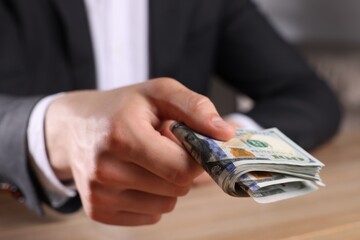 Wall Mural - Money exchange. Man holding dollar banknotes at wooden table, closeup