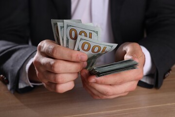 Wall Mural - Money exchange. Man counting dollar banknotes at wooden table, closeup