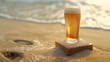 Beer glass on a square stone stand with sea waves in the background. Alcoholic or non-alcoholic drink on pedestal in the sandy beach.
