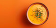 A plate of seasonal cream soup from carrot or pumpkin on orange background. The soup is garnished with parsley and pepper.