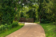 A pathway in an urban park, crossing a quaint bridge with metal railings. The path is embraced by an array of green hues from trees and shrubs in the Texas Hill Country