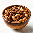A wooden bowl filled with various types of nuts, placed on a white surface.