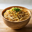 A wooden bowl filled with spaghetti, topped with green herbs, placed on a table.