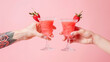 Two people are holding up two glasses cocktail with strawberry. Two hands toasting with two strawberry margaritas cocktail on pink background