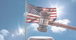 A gavel in front of American flag waving against sunny sky