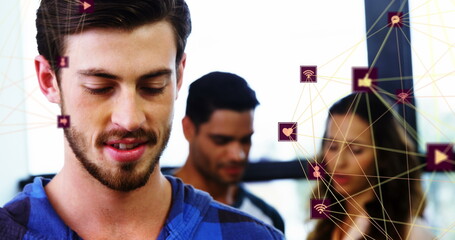 Sticker - Image of two globes of digital icons over caucasian man smiling while using smartphone at office