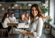 © PixelStock - businesswoman smiling while holding a tablet in an office with a team working at a table