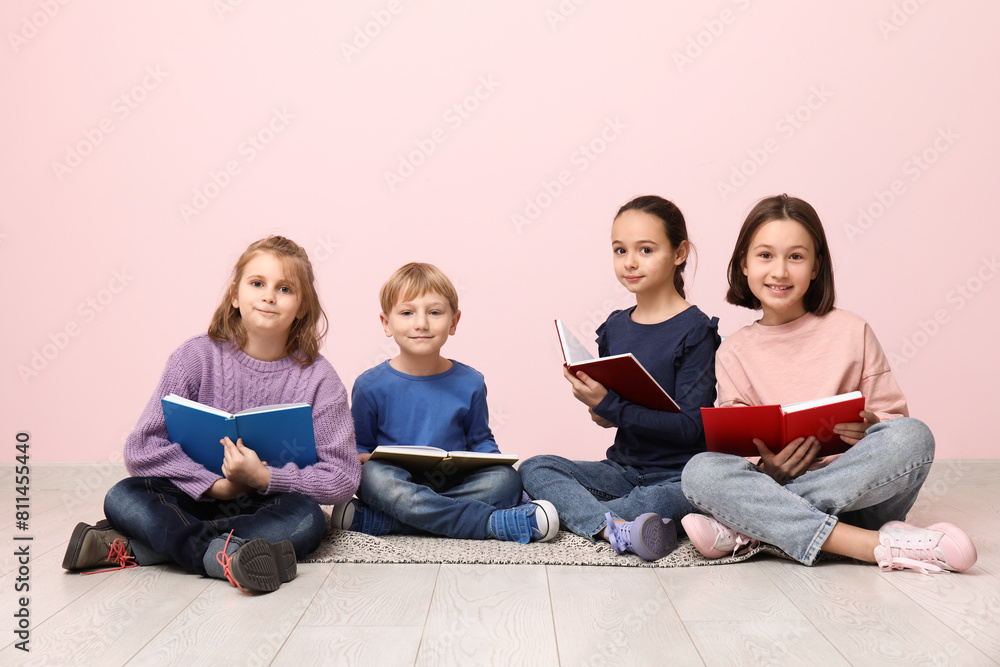 Little children reading books while sitting on floor near pink wall