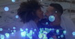 Image of glowing blue spots falling over african american couple embracing each other at beach