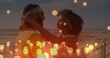 Image of glowing yellow spots over african american couple embracing each other at the beach