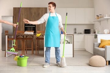 Wall Mural - Young man taking floor mop from woman in kitchen