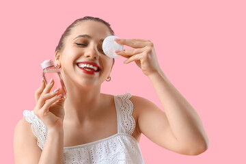 Wall Mural - Young woman with micellar water and cotton pad on pink background, closeup