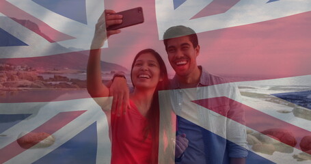 Wall Mural - Image of flag of uk flag over happy diverse couple taking selfie by sea