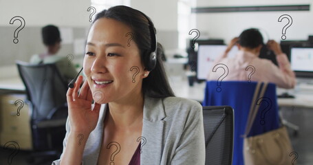 Sticker - Image of question mark symbols over asian woman talking over headphones at office