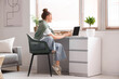 © Pixel-Shot - Young woman sitting at workplace and working with laptop in living room