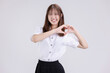 Pretty Asian woman in university student uniform make heart shape hand signal over isolated white background.