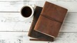 Leather notebooks and a cup of coffee placed on a white wooden surface from above