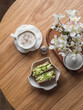 Breakfast served, brunch table - cappuccino and avocado, eggs, micro greens toast on a round wooden table, top view. Aesthetic food concept